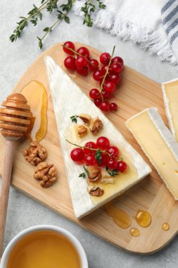 Brie cheese served with red currants, walnuts and honey on light table, flat lay