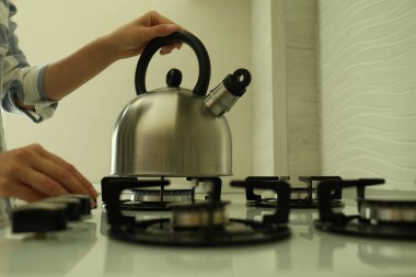Woman putting kettle on gas stove in kitchen, closeup