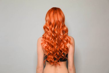 Beautiful woman with long orange hair on light grey background, back view