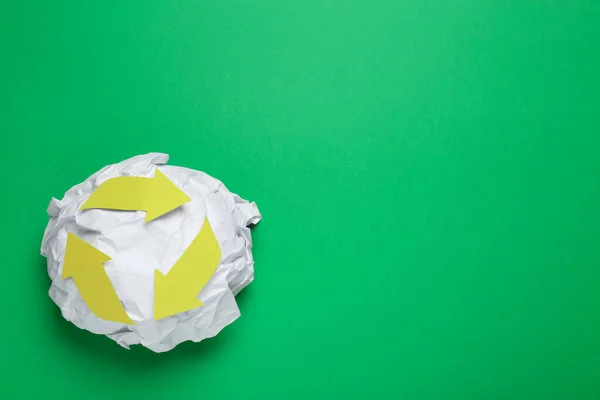 Crumpled paper with recycling symbol on green background, top view. Space for text