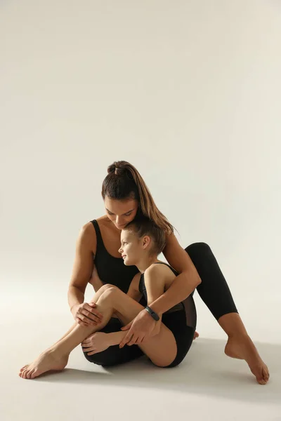 Little gymnast and her coach sitting on white background