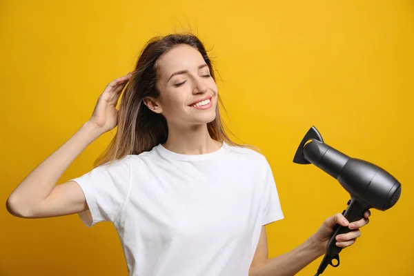 Hermosa Mujer Joven Usando Secador Pelo Sobre Fondo Amarillo — Foto de Stock