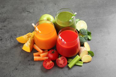 Farklı lezzetli meyve suları ve gri masada taze malzemeler.