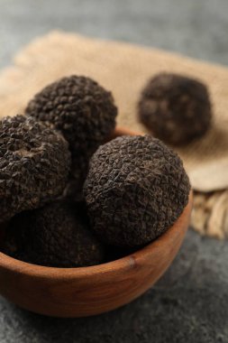 Black truffles in wooden bowl on grey table, closeup