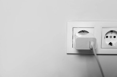 Charger adapter plugged in power socket indoors, closeup. Space for text