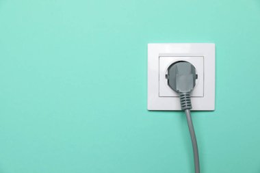 Power socket with inserted plug on turquoise wall, space for text. Electrical supply