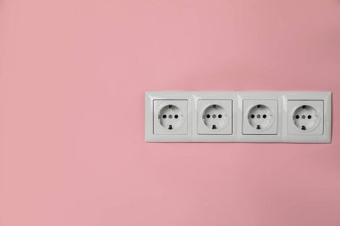 Power sockets on pink wall, space for text. Electrical supply