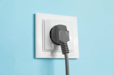 Power socket with inserted plug on light blue wall, closeup. Electrical supply