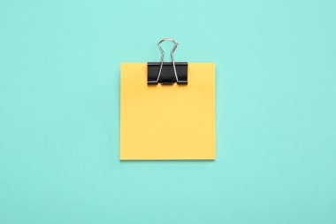 Turkuaz arka planda siyah kağıt kıskacı olan boş turuncu bir not, üst manzara. Metin için boşluk