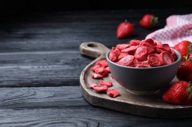 Freeze dried and fresh strawberries on black wooden table. Space for text