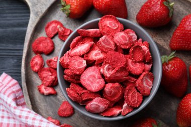 Freeze dried and fresh strawberries on black wooden table, top view
