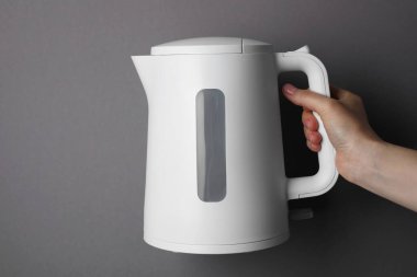 Woman holding modern electric kettle on grey background, closeup
