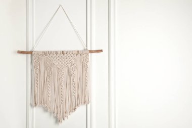 Stylish beige macrame hanging on white wall. Space for text