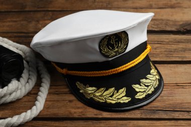 Peaked cap and rope with binoculars on wooden background