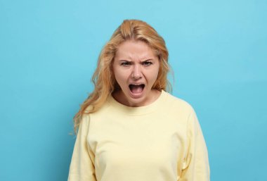 Aggressive young woman screaming with rage on light blue background