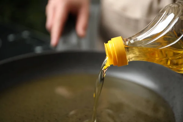 Woman pouring cooking oil from bottle into frying pan, closeup