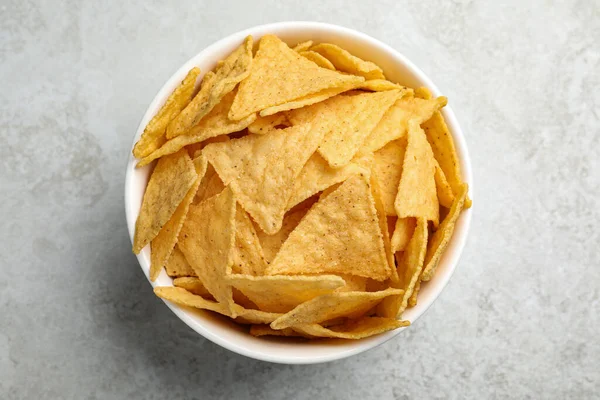 Bowl with tasty tortilla chips (nachos) on grey table, top view