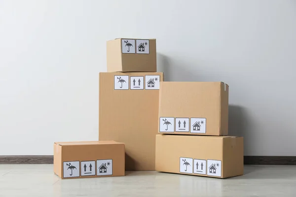 Many closed cardboard boxes with packaging symbols on floor near white wall. Delivery service