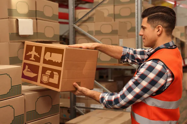 Worker stacking cardboard boxes with shipping icons in warehouse. Wholesaling