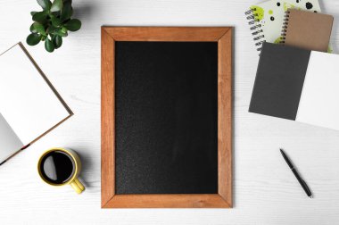 Clean small chalkboard, coffee, plant and stationery on white wooden table, flat lay