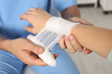 Doctor applying bandage onto patient's wrist in hospital, closeup