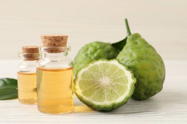 Glass bottles of bergamot essential oil and fresh fruits on white wooden table