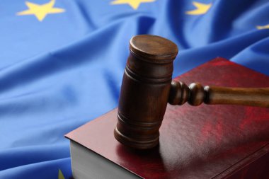 Wooden judge's gavel and book on flag of European Union, closeup. Space for text