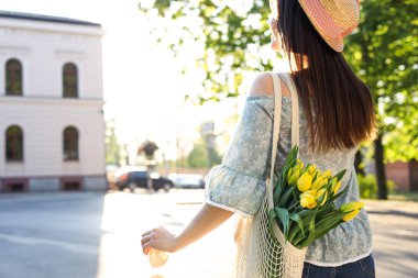 Young woman with bouquet of yellow tulips on city street, back view. Space for text