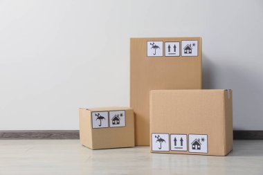 Many closed cardboard boxes with packaging symbols on floor near white wall. Delivery service