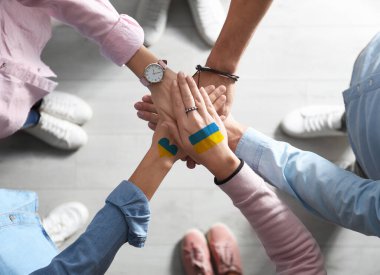 Help for Ukraine. People holding hands together with drawings of Ukrainian flag, top view