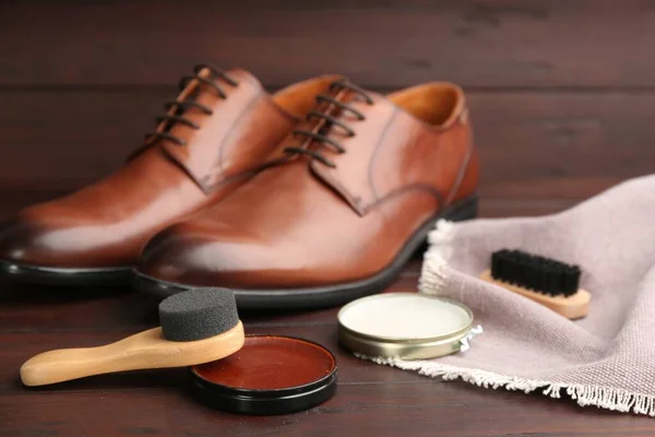 Shoe care products and footwear on wooden table, closeup