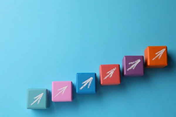 Colorful wooden cubes with chalked arrows on light blue background, flat lay and space for text. Management concept