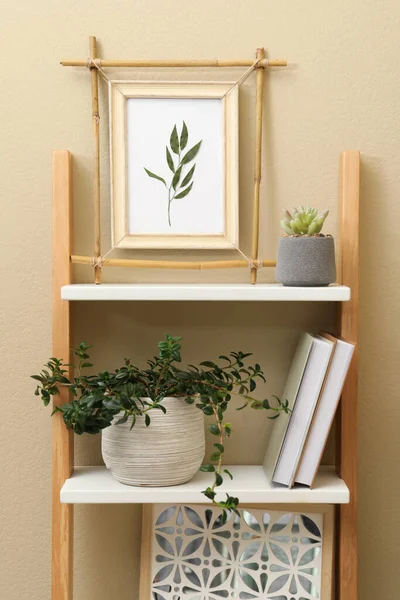 Bamboo frame and different decor elements on shelving unit near beige wall