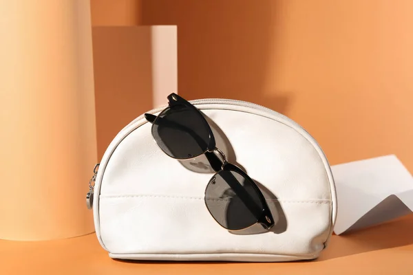 Stylish sunglasses and white makeup bag on pale orange background