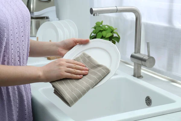 Woman wiping plate with towel near sink in kitchen, closeup