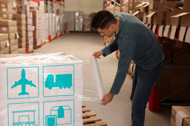 Worker wrapping boxes with shipping icons in stretch film at warehouse