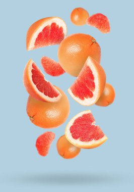Tasty ripe grapefruits falling on light background