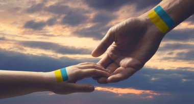 Help for Ukraine. Man and child holding hands with drawings of Ukrainian flag and beautiful sky with clouds at sunset on background, closeup. Banner design