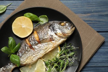 Delicious roasted fish with lemon on blue wooden table, top view