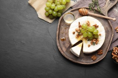 Brie cheese served with grapes, walnuts and honey on grey table, flat lay. Space for text