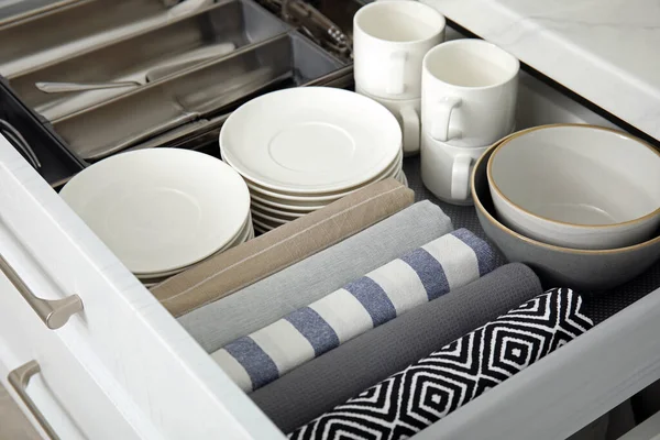 Open drawer of kitchen cabinet with different dishware and towels, closeup