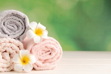 Closeup view of soft folded towels and plumeria flowers on white wooden table, space for text