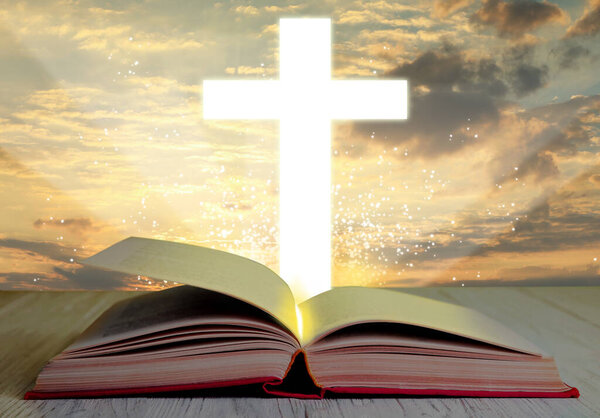 Silhouette of cross and open Bible on white wooden table at sunrise