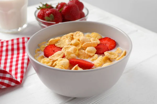 Corn flakes with strawberries in bowl served on white wooden table, closeup