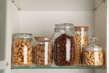 Rafta farklı kahvaltı gevrekleri olan cam kaplar.