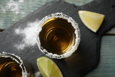 Mexican Tequila shots, lime slices and salt on blue wooden table, top view