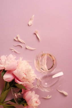 Glasses with rose wine and beautiful peonies on pink background, flat lay