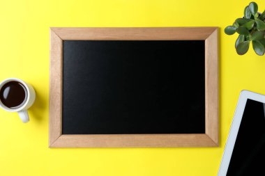 Clean small chalkboard, coffee, plant and tablet on yellow background, flat lay
