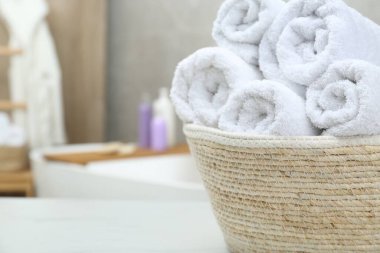 Wicker basket with rolled bath towels on white table in bathroom, closeup. Space for text