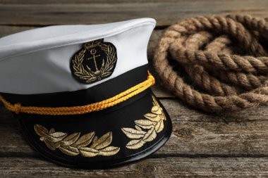 Peaked cap with accessories and rope on wooden background, closeup
